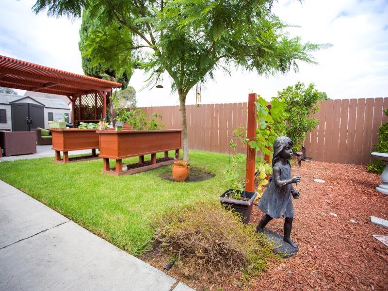A well-maintained backyard garden featuring a patio area, lush greenery, and a decorative statue.