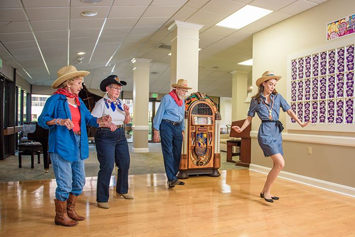 A group of people wearing cowboy-themed attire dancing indoors.