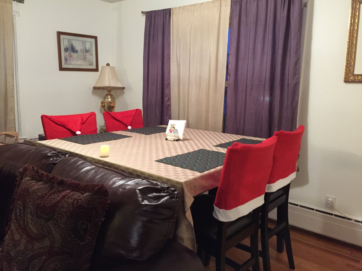 A dining room with a large table covered in a tablecloth, surrounded by chairs with red covers.