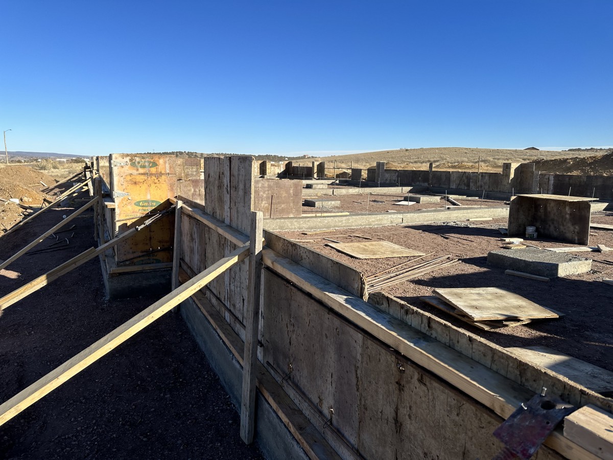 A construction site with concrete forms set up for a building foundation under a clear blue sky.