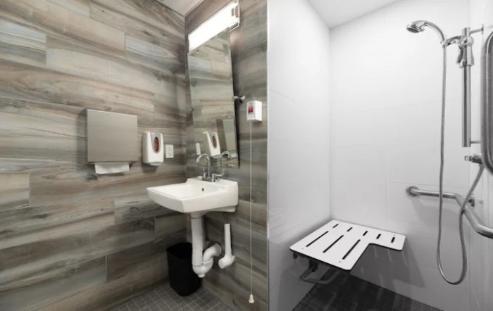 A modern, accessible bathroom with a wall-mounted sink and folding chair.
