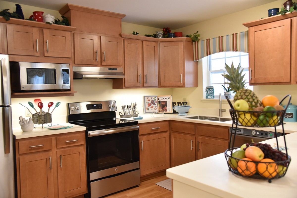 A modern kitchen with wooden cabinets, stainless steel appliances, and a fruit basket on the counter.