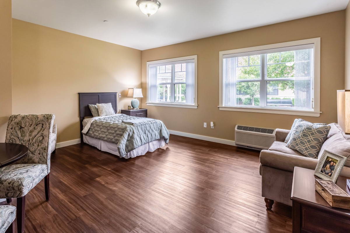 A spacious bedroom with a single bed, hardwood floors, and large windows letting in natural light.