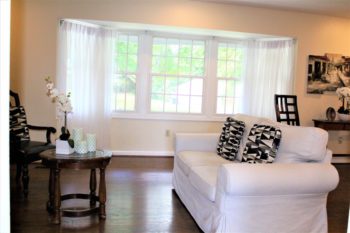 A bright and airy living room with a large window, white sofa, and geometric cushions.