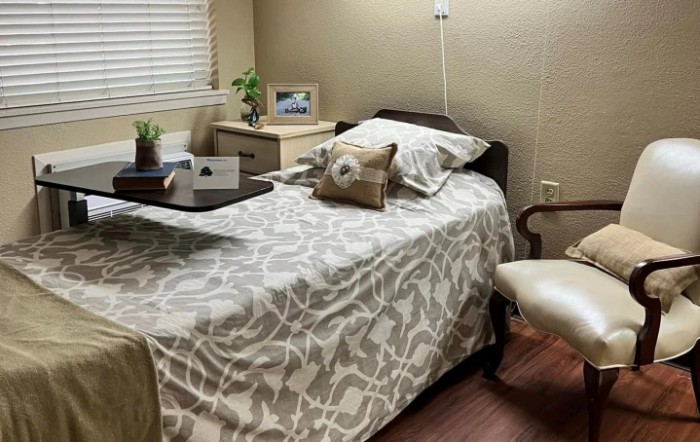 A cozy bedroom with a single bed, decorated with patterned bedding and pillows, alongside a wooden side table, chair, and lamp.