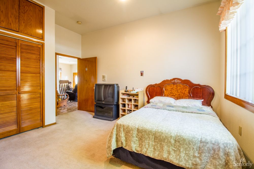 A cozy bedroom with a large bed, wooden headboard, vintage television, and nightstand.