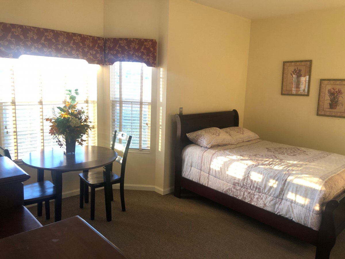 A cozy bedroom featuring a bed, a small table with chairs, and a bouquet of flowers by the window.