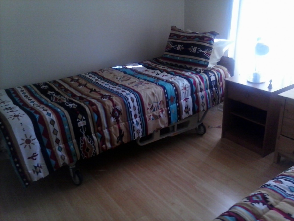 A cozy bedroom with a single bed covered in a patterned quilt next to a desk by the window.