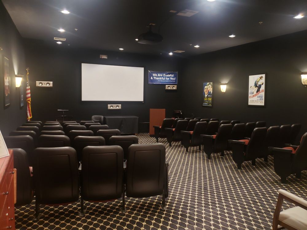 An empty theater room with rows of seats facing a large screen.
