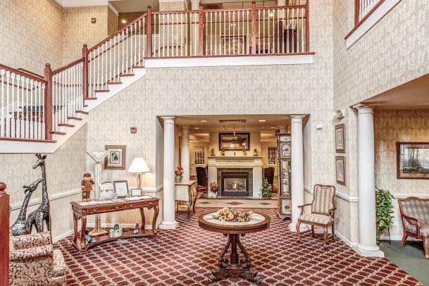 A cozy hotel lobby with a central table, elegant decor, and a staircase leading to the upper level.