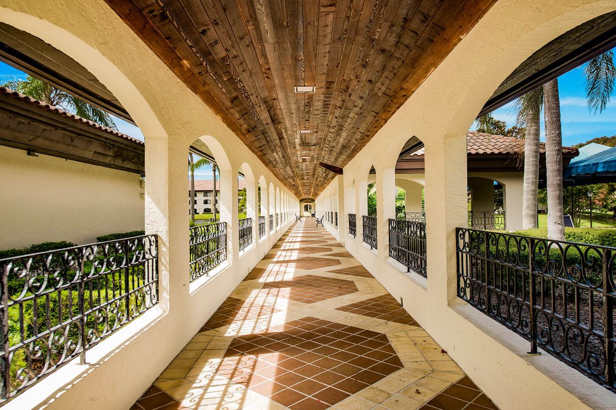 A beautifully symmetrical corridor with arched openings, a wooden ceiling, and patterned tiles, showcasing intricate play of sunlight and shadows.