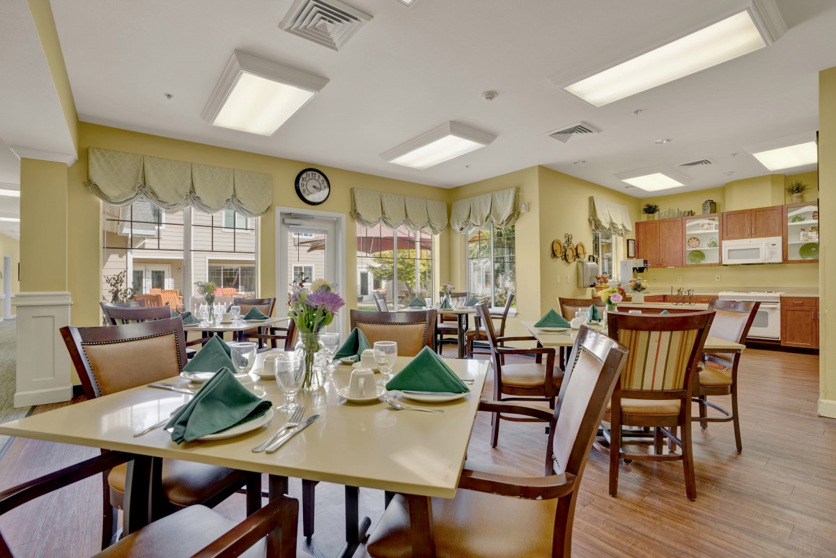 A cozy dining room setup with neatly arranged tables, green napkins, and comfortable seating.