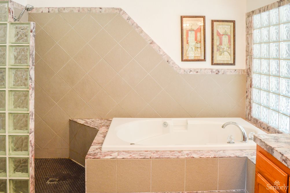 A bathroom interior featuring a tiled bathtub with two framed artworks on the wall.