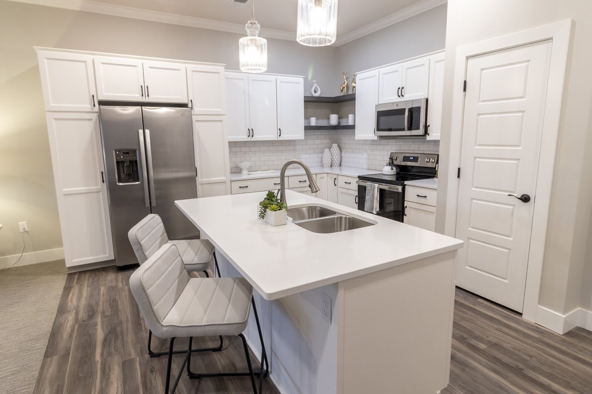 A modern kitchen with white cabinets and stainless steel appliances, featuring a central island with bar stools and pendant lighting.