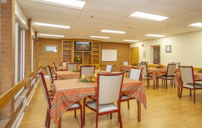 An indoor dining room with multiple tables and chairs, featuring tablecloths and wooden furniture.