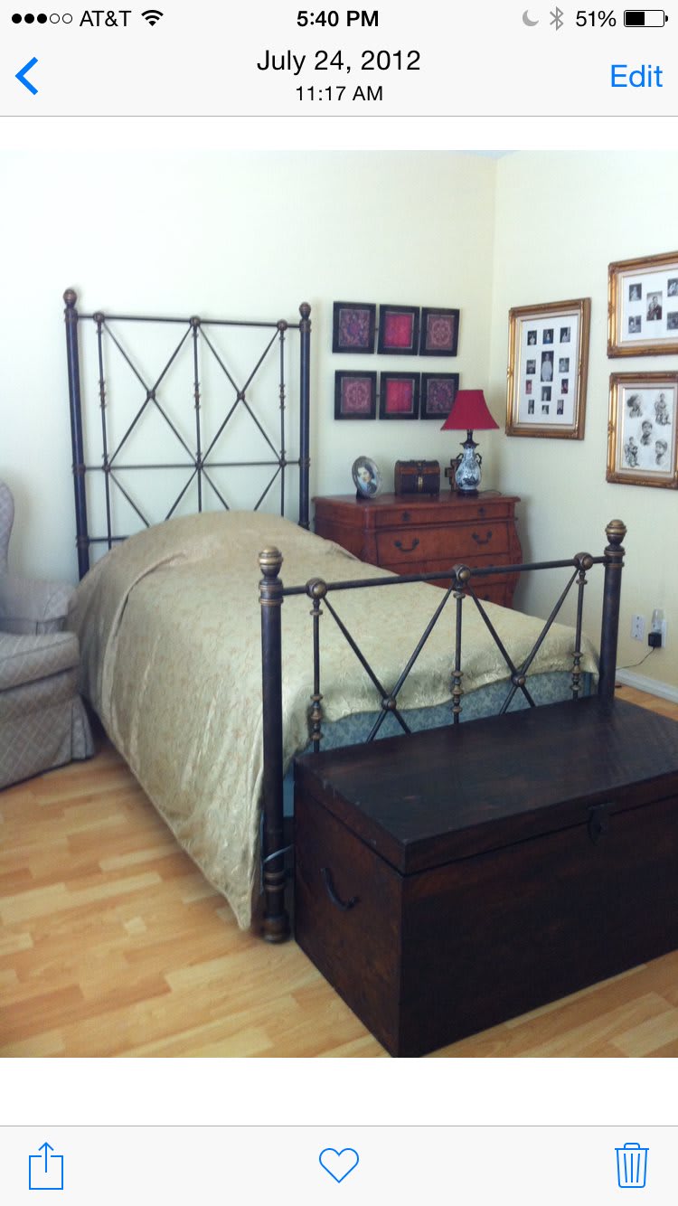 A cozy bedroom featuring a metal-framed bed with a gold comforter, surrounded by framed pictures and wooden furniture.