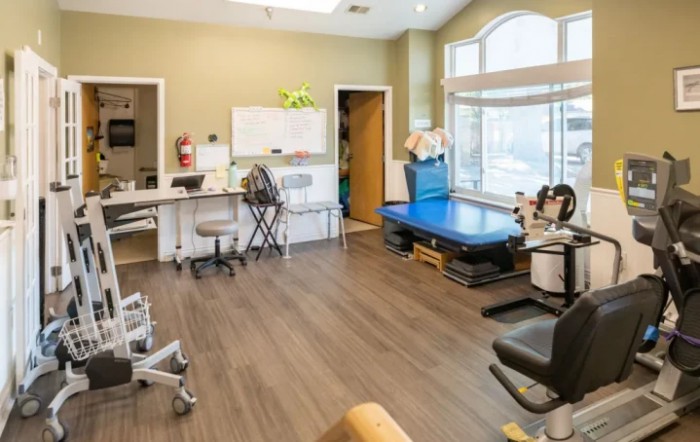 A bright and organized rehabilitation clinic workspace featuring medical equipment, desks, and chairs.