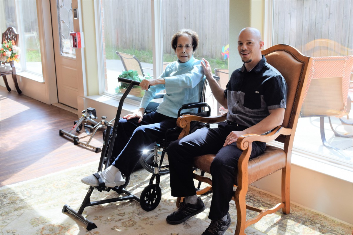 Two seniors engage in a physical therapy session indoors, using an exercise machine aimed at rehabilitation.