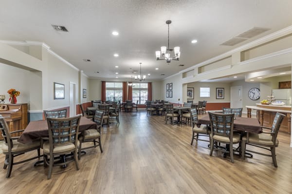 A spacious dining area with neatly arranged tables and chairs, featuring elegant lighting and wooden flooring.