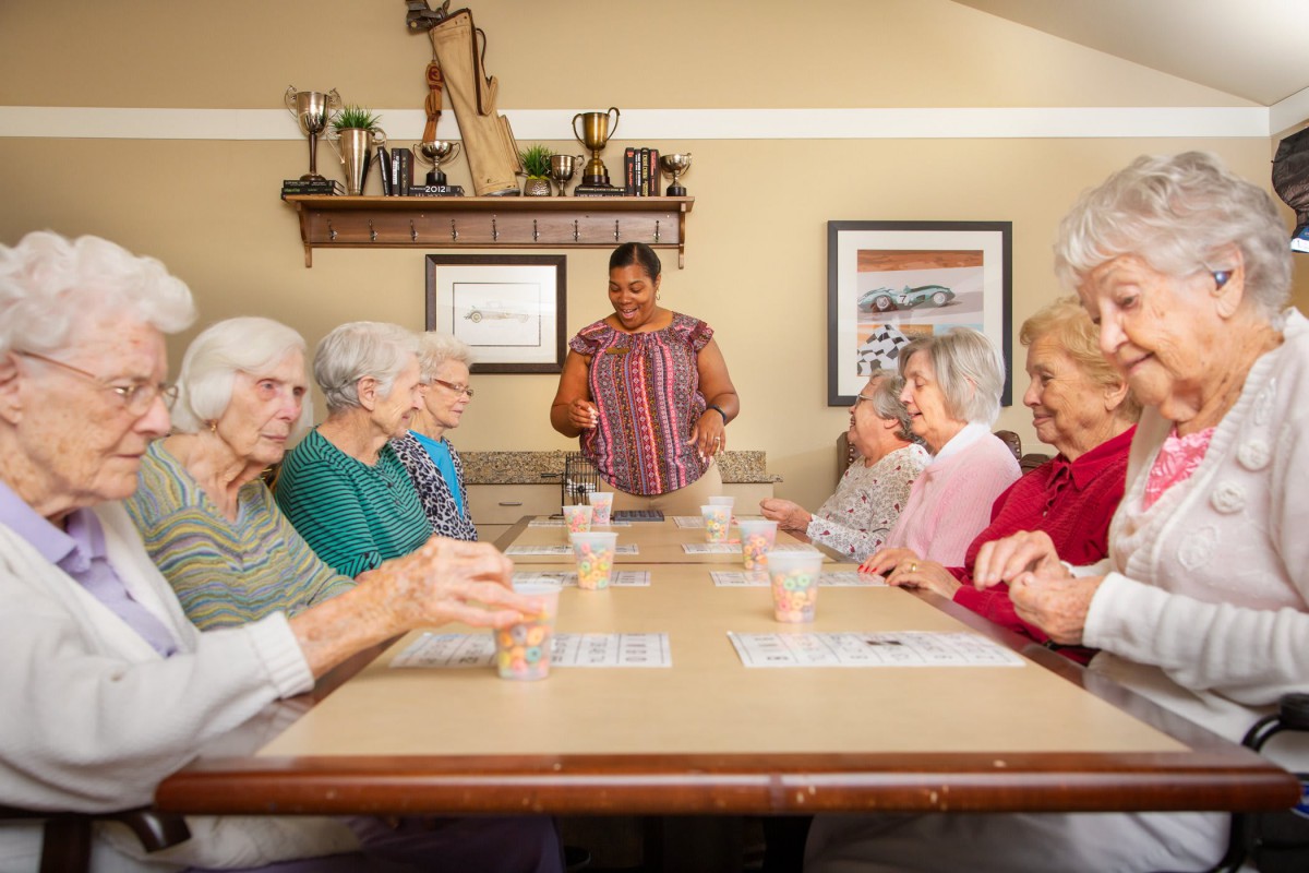 A group of seniors sitting around a table, engaged in conversation with a caregiver.