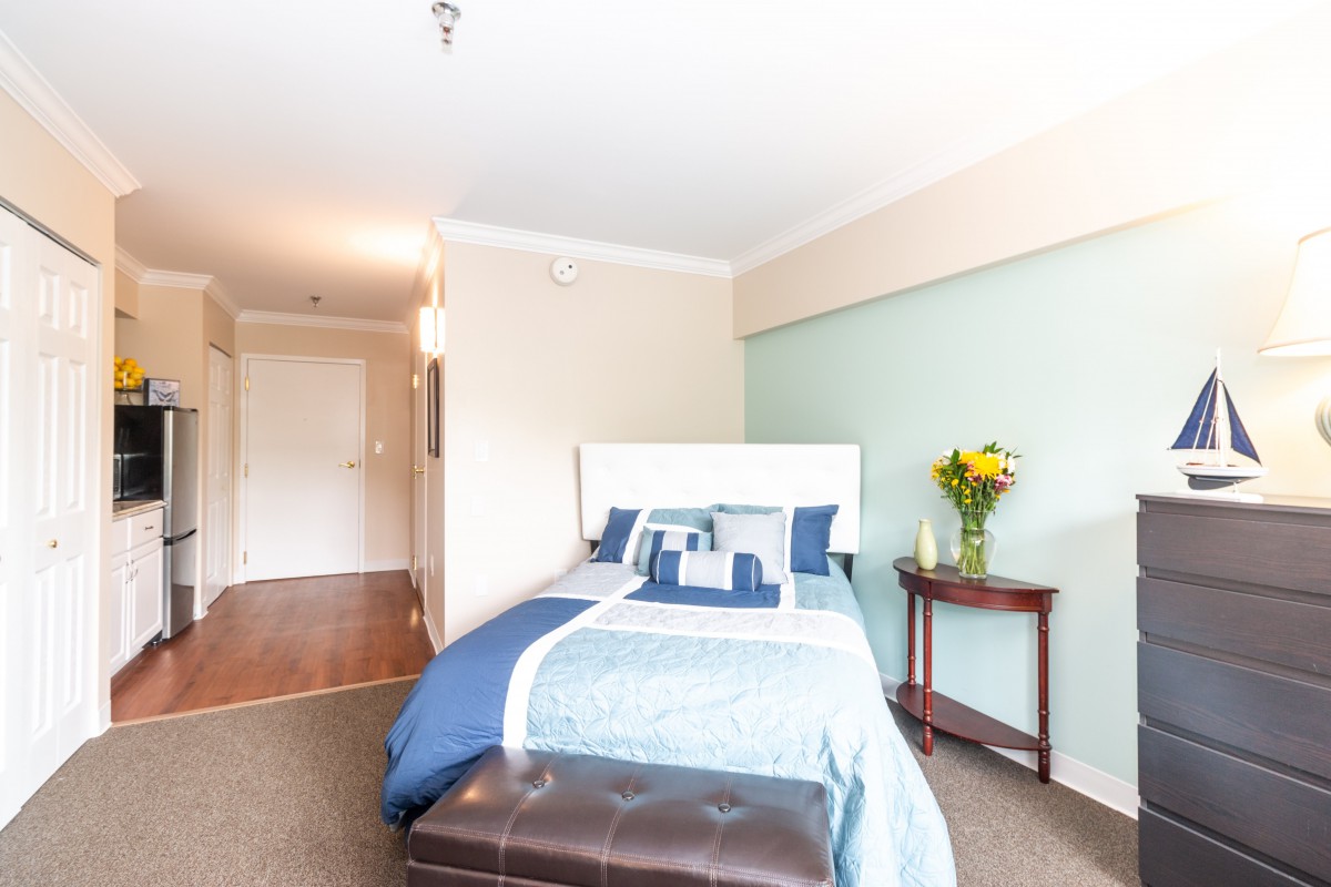 A bright, cozy bedroom featuring a bed with blue and white bedding and a small table with a vase of flowers.