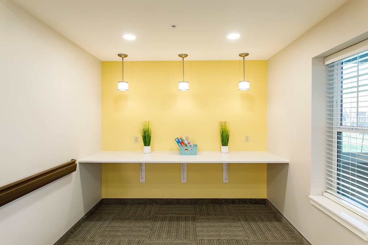 A modern, minimalist workspace featuring a yellow accent wall with hanging pendant lights and decorative plants.