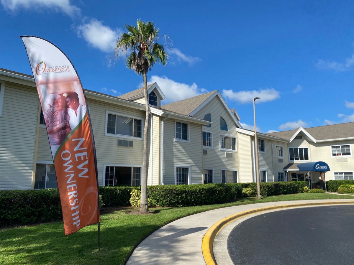 A sunny day view of a residential building with palm trees and a welcoming banner.