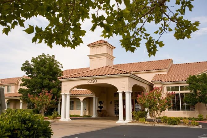 A scenic view of a building entrance with columns and a tiled roof surrounded by trees.