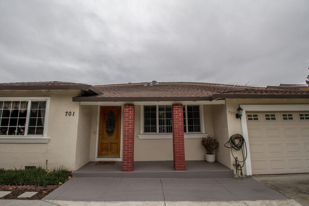 A small residential house with brick pillars at the entrance under a cloudy sky.