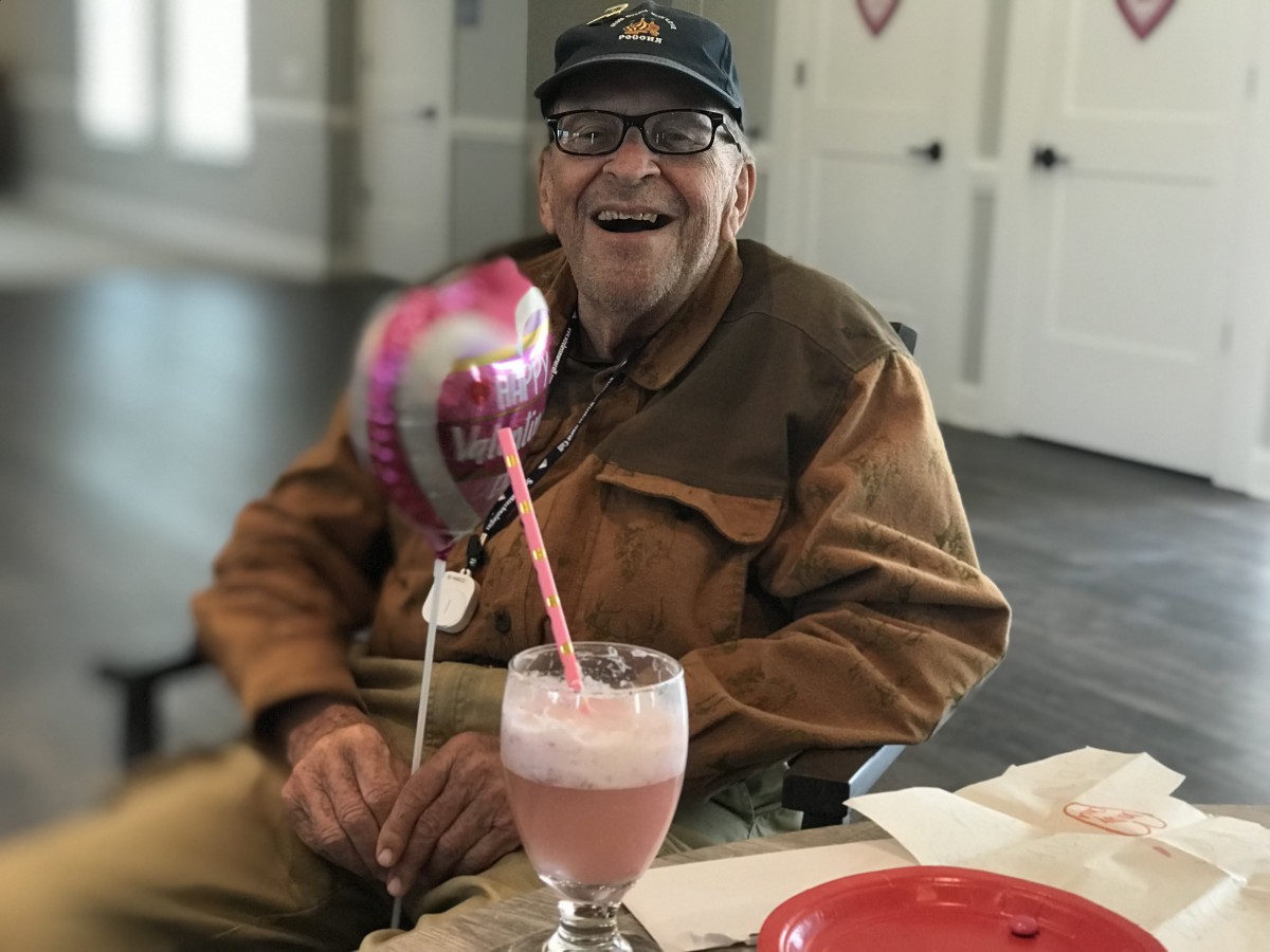 An elderly man joyfully celebrates with a pink balloon and a milkshake.