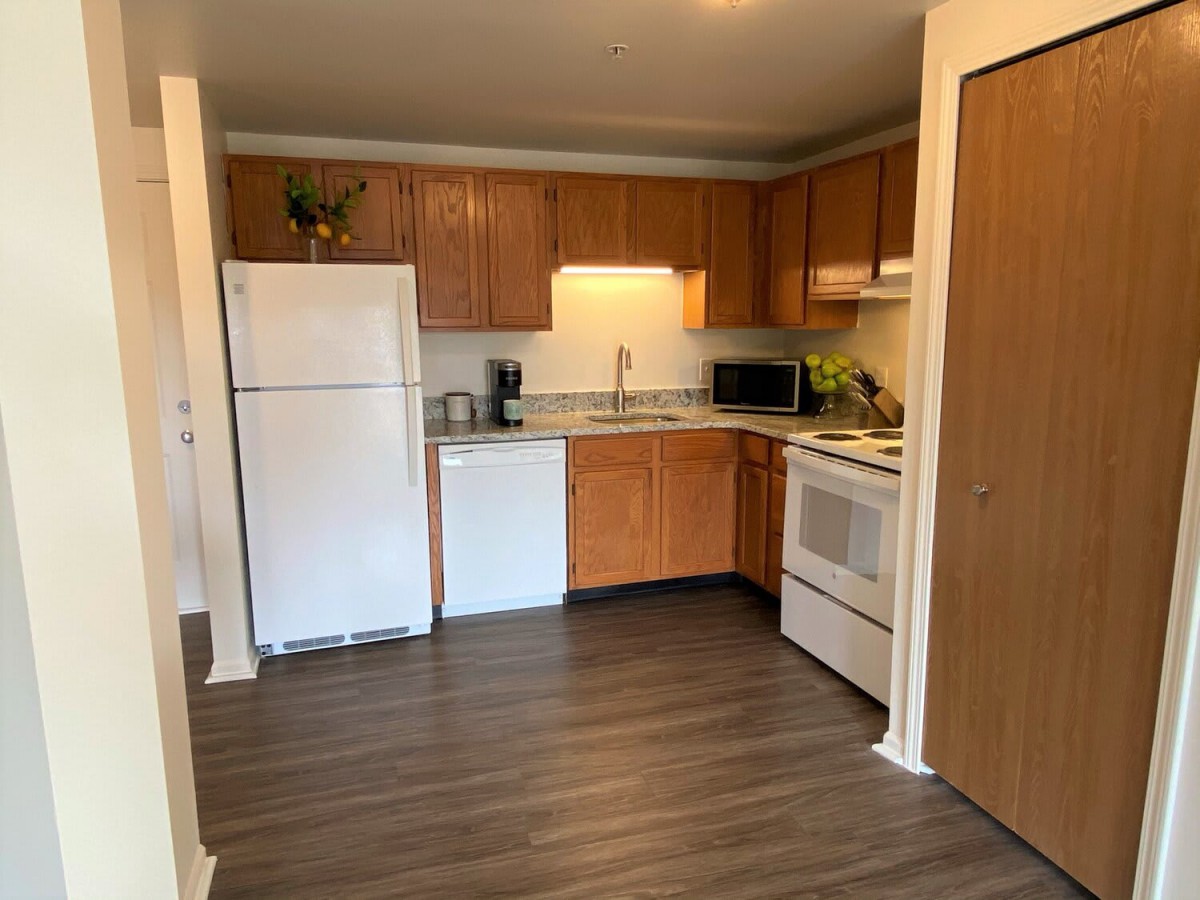 A modern kitchen with wooden cabinets, equipped with a refrigerator, dishwasher, oven, and microwave.