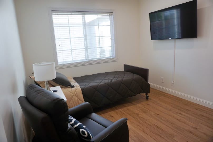 A minimalist bedroom with a single bed, wall-mounted television, and armchair.