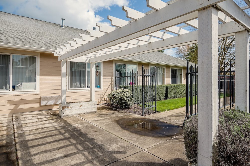 A sunny view of a house patio with a pergola and fenced yard.