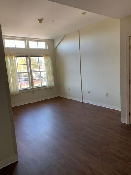 An empty room with wooden flooring and large windows allowing natural light.