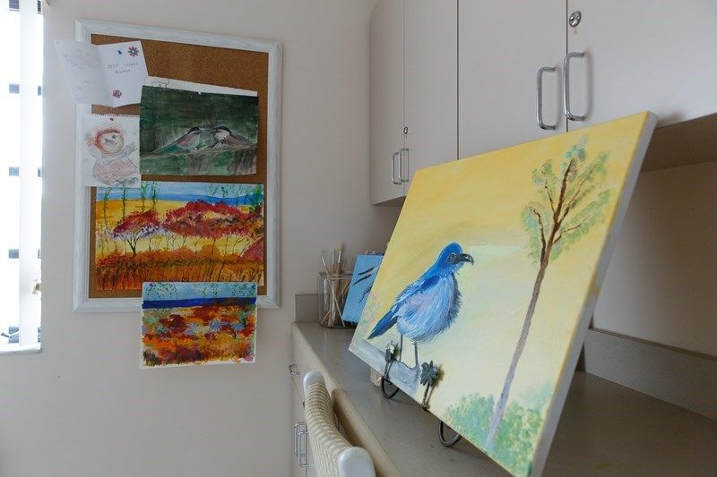 A cozy art studio displaying a painting of a blue bird on a canvas alongside other landscape artworks.