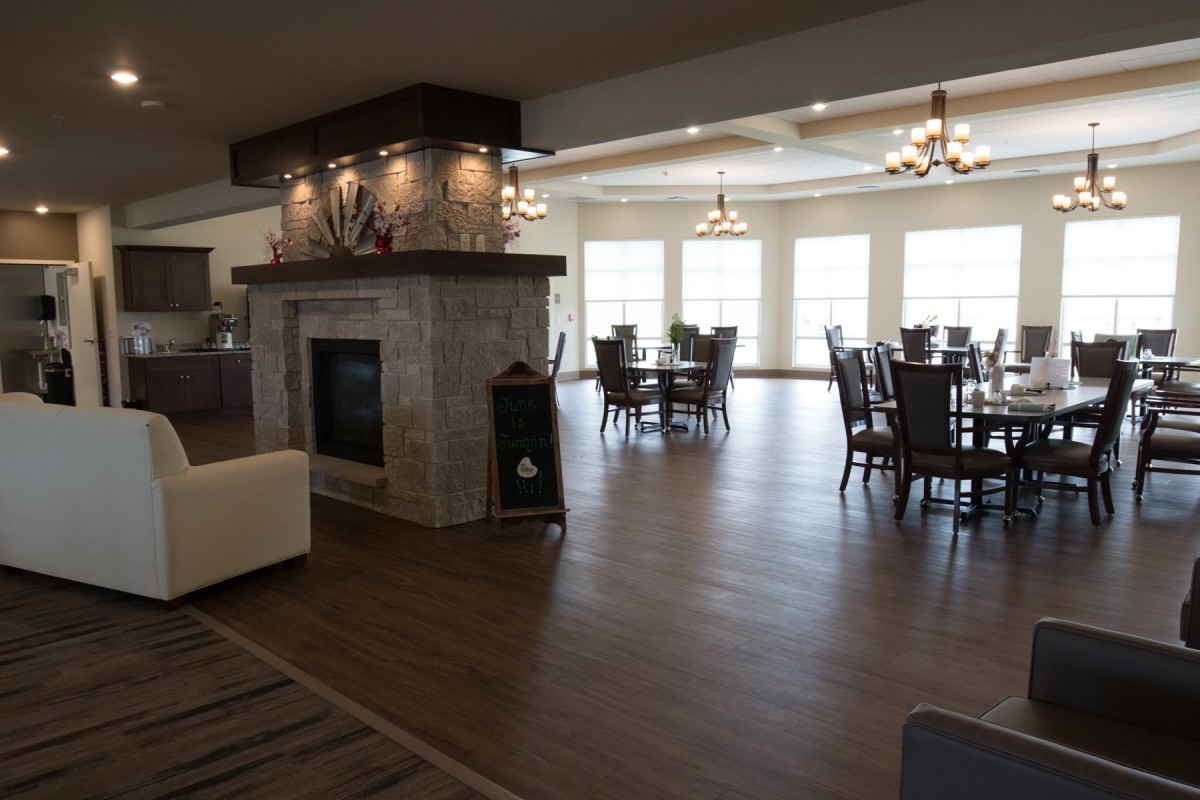 A spacious dining area with a fireplace, hardwood floors, and multiple tables and chairs flooded with natural light from large windows.