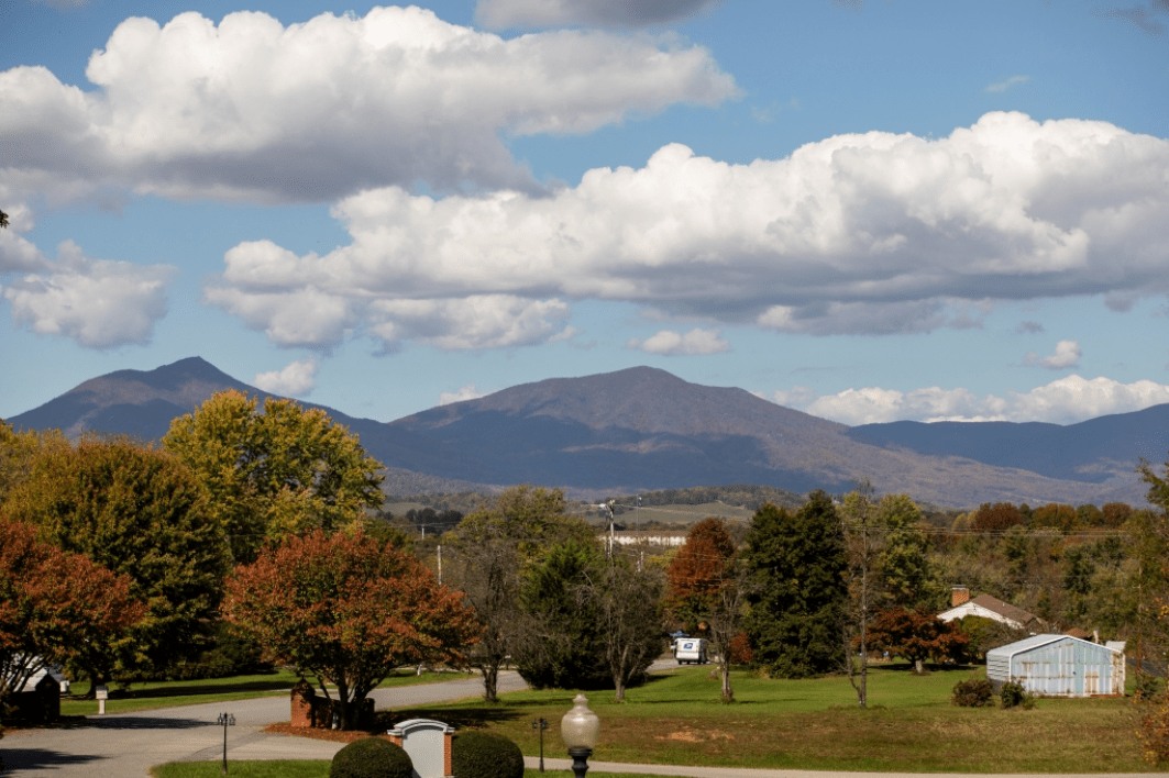 A scenic landscape with mountains in the distance under a partly cloudy sky, surrounded by trees and open land.