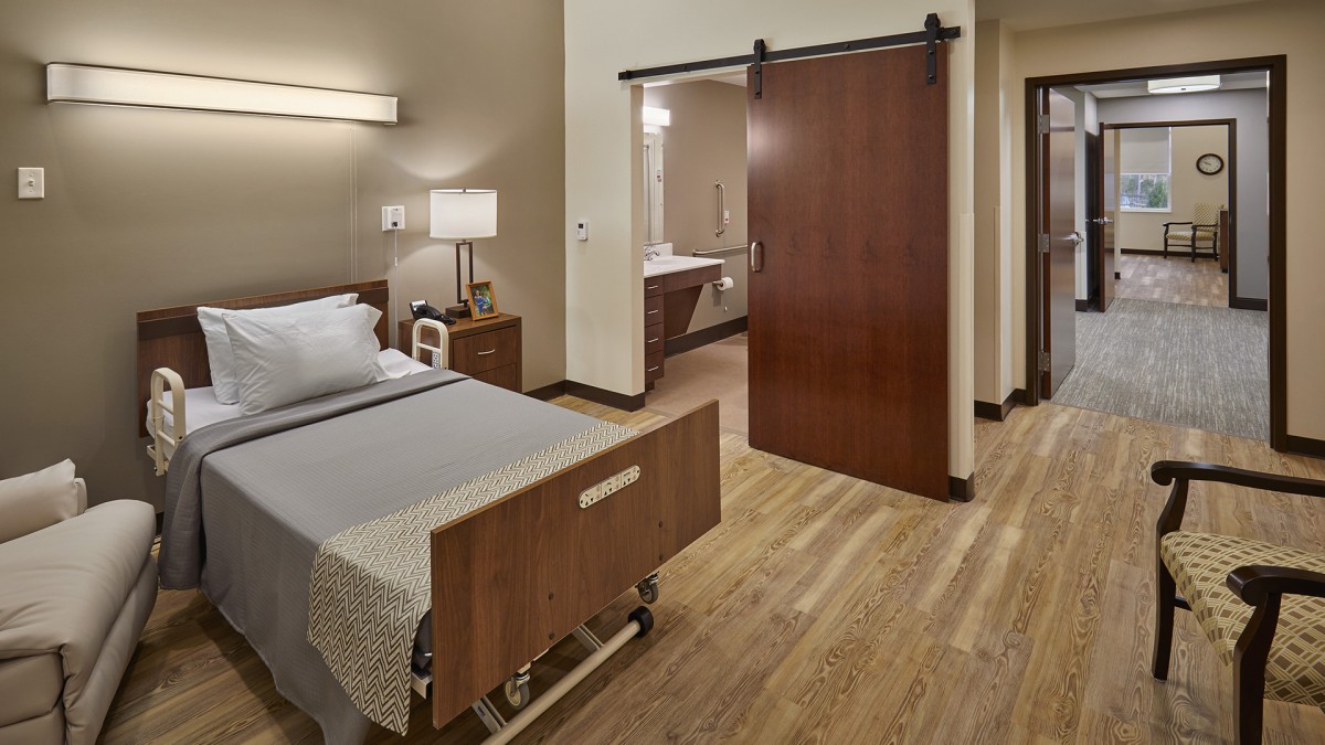A hospital room featuring a single bed with modern furnishings and a wooden sliding door.