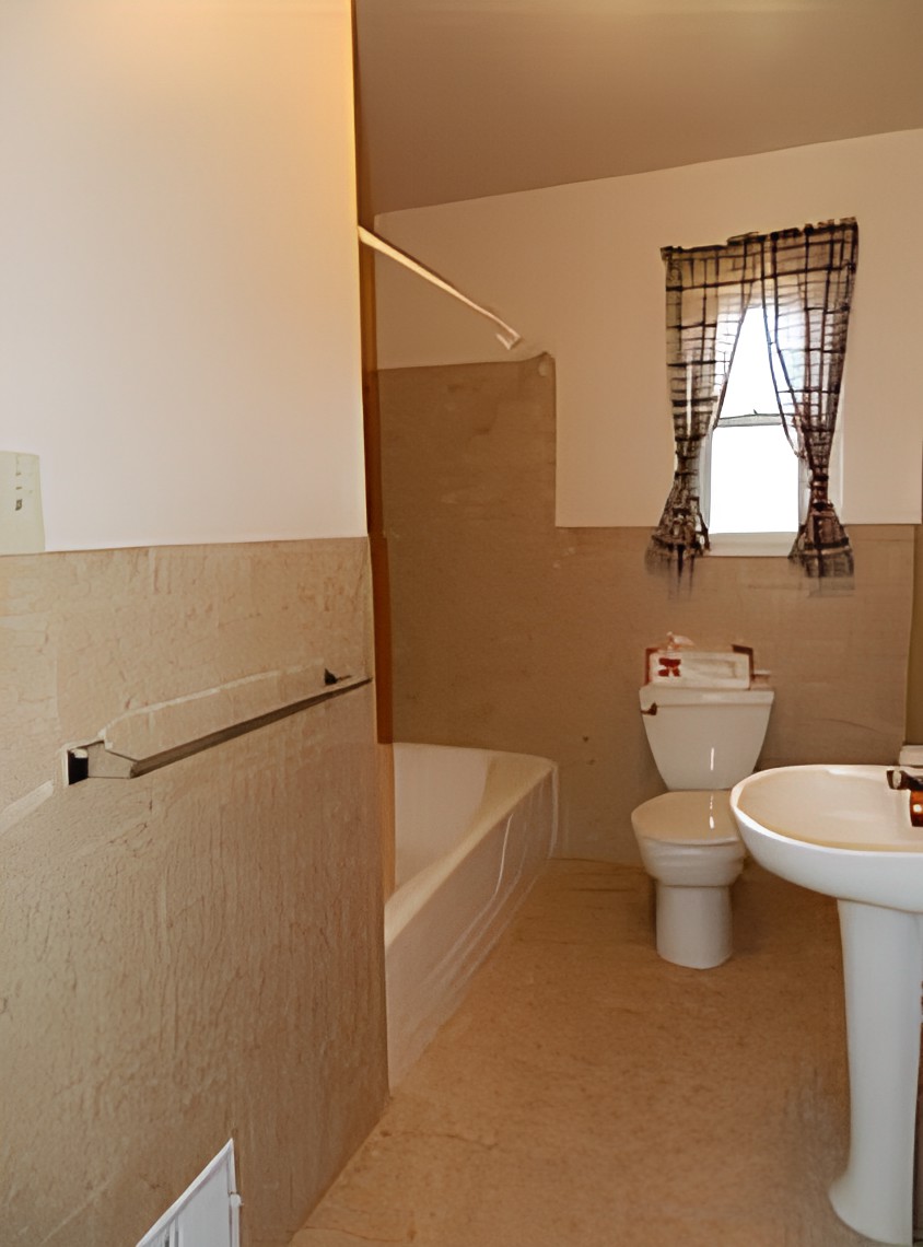 A simple bathroom with a bathtub, toilet, and pedestal sink, featuring tiled walls and a window with plaid curtains.