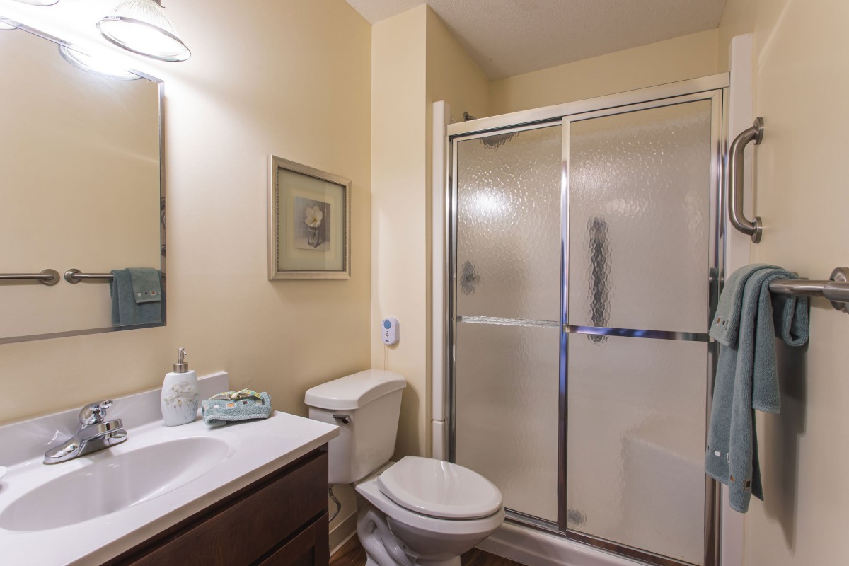 A neat and tidy bathroom featuring a glass-enclosed shower, sink with mirror, and toilet.