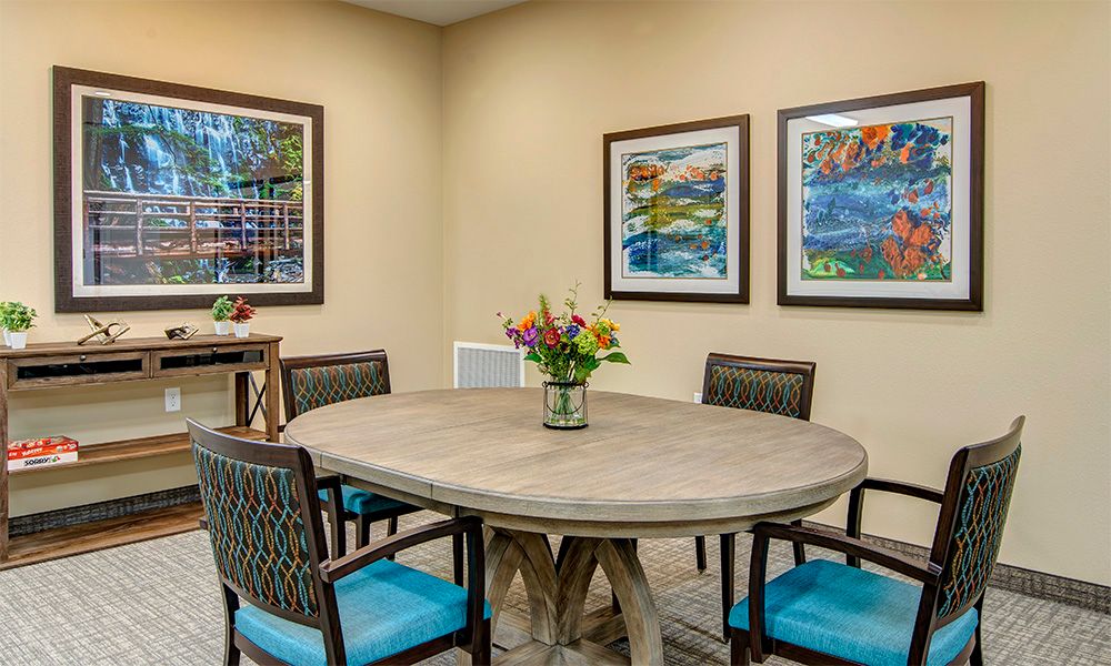 A cozy dining room with a round table, six chairs, and colorful artwork on the walls.