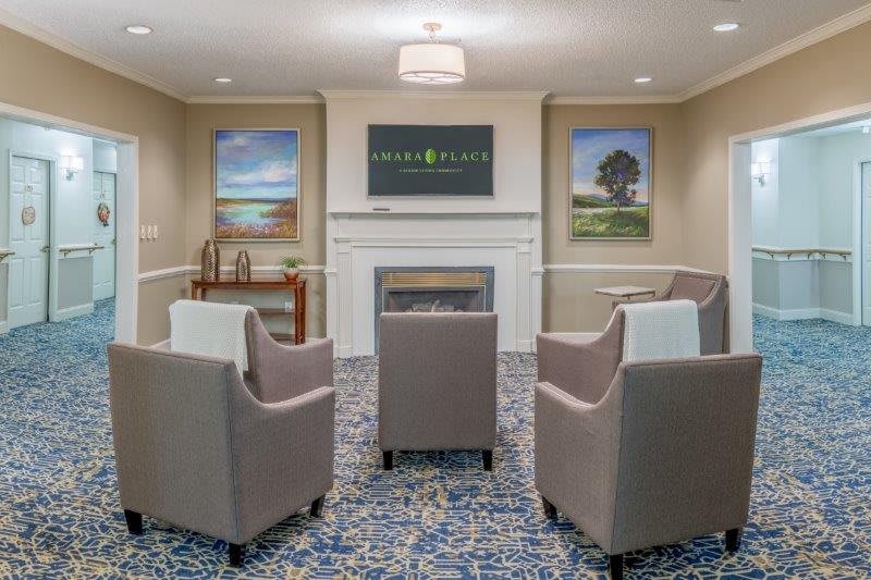 A cozy living room with armchairs arranged around a fireplace, decorated with paintings and a patterned carpet.