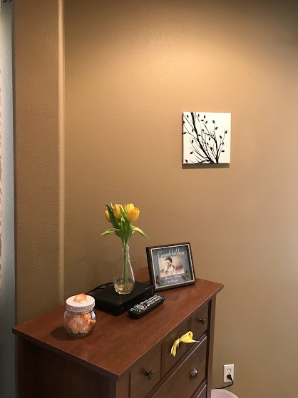 A minimalist interior space featuring a small wooden table with a vase of yellow flowers, a photo frame, and wall art.