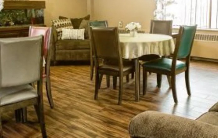 A cozy dining and living area with wooden flooring, featuring a table with chairs and a sofa in the background.