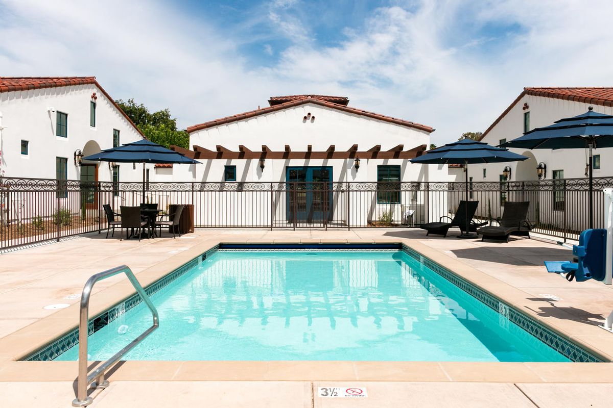 Outdoor swimming pool with lounge chairs and blue umbrellas at a residential complex.