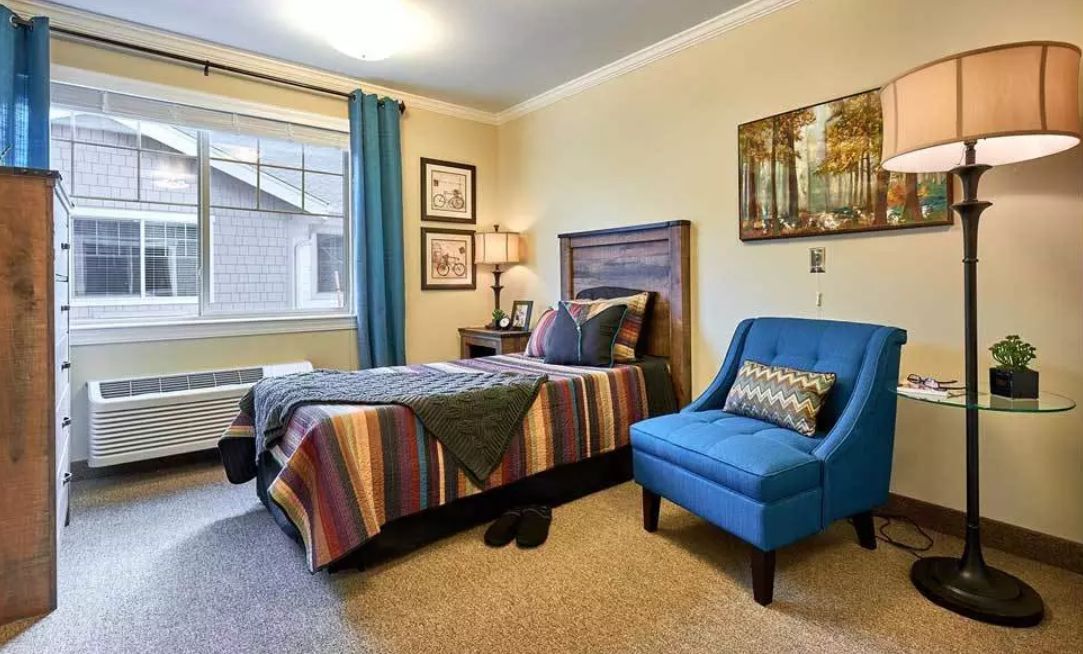 A cozy bedroom with a colorful bedspread, blue accent chair, and decorative artwork.