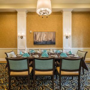 An elegantly decorated dining room with a set table and plush chairs, featuring a central chandelier and artwork on the wall.