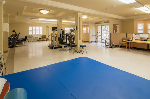 A spacious rehabilitation gym equipped with exercise machines and a blue mat for therapy activities.
