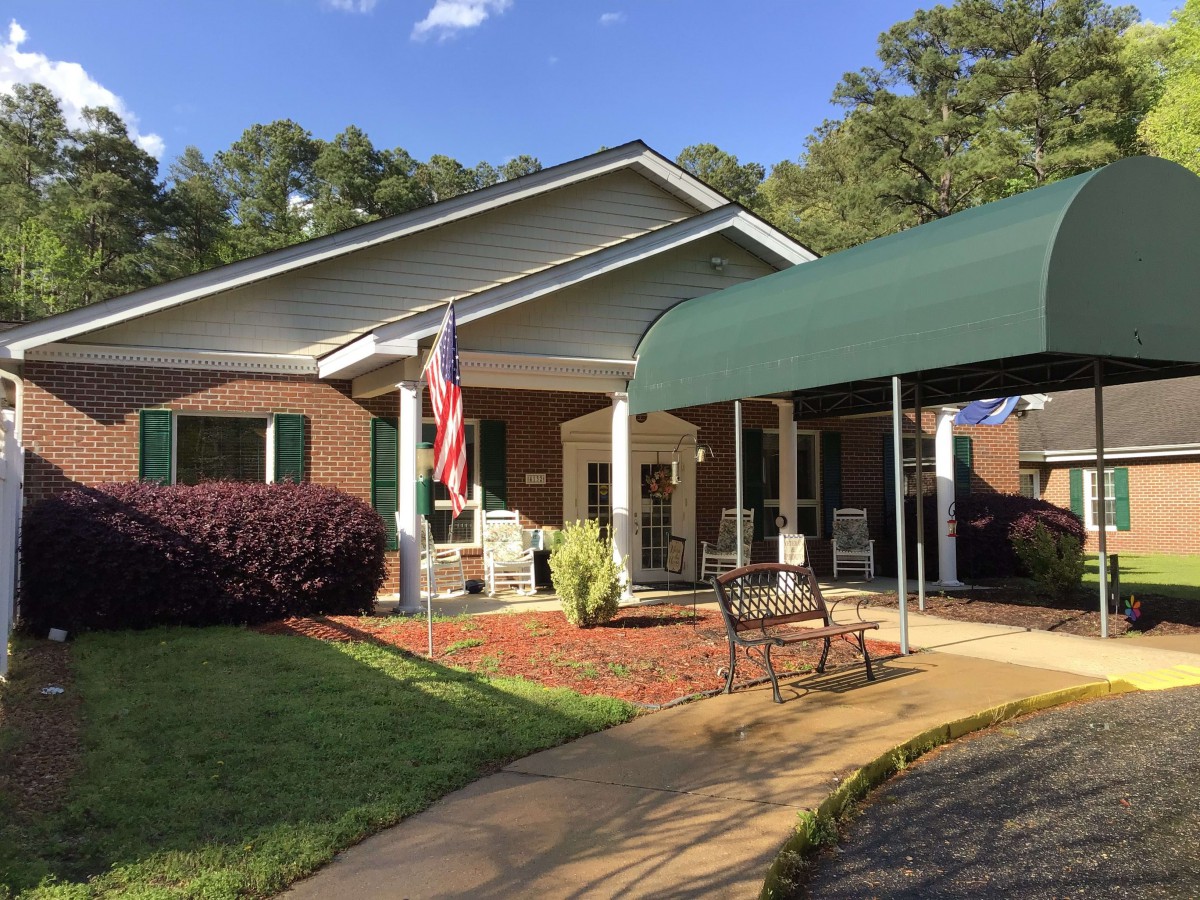 A building entrance with a green awning, seating area, and flag.