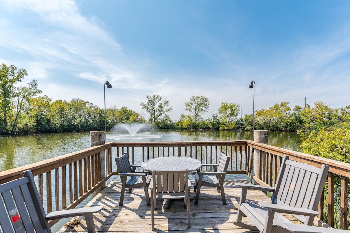 A peaceful deck with wooden seating overlooking a lake with fountains.